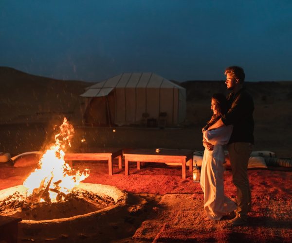 Couple hug in love near big campfire. Romantic night in glamping desert camp in Sahara, Morocco. Honeymoon.